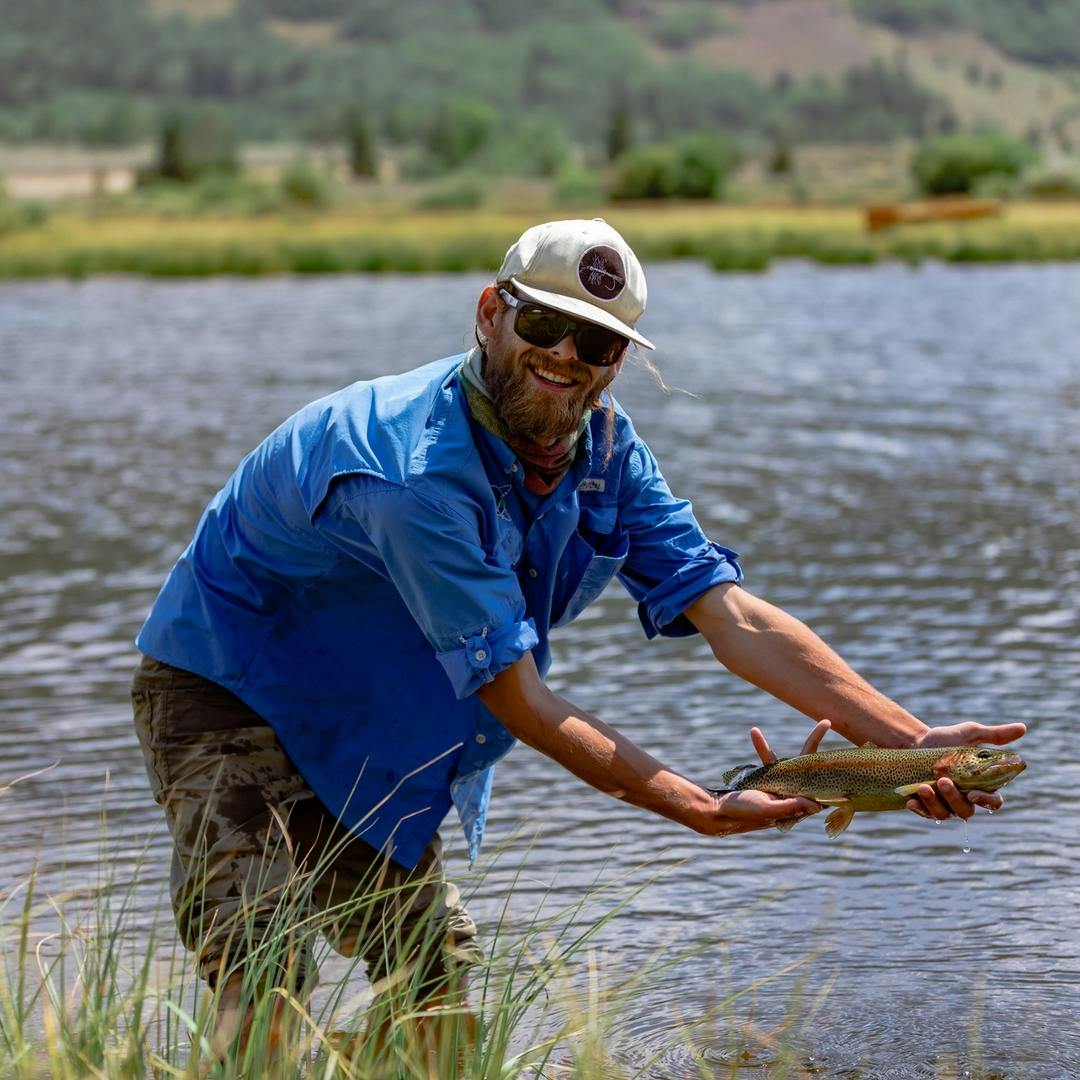 A Nova Guide fish flying guide holding a trout in front of a lake in Vail.